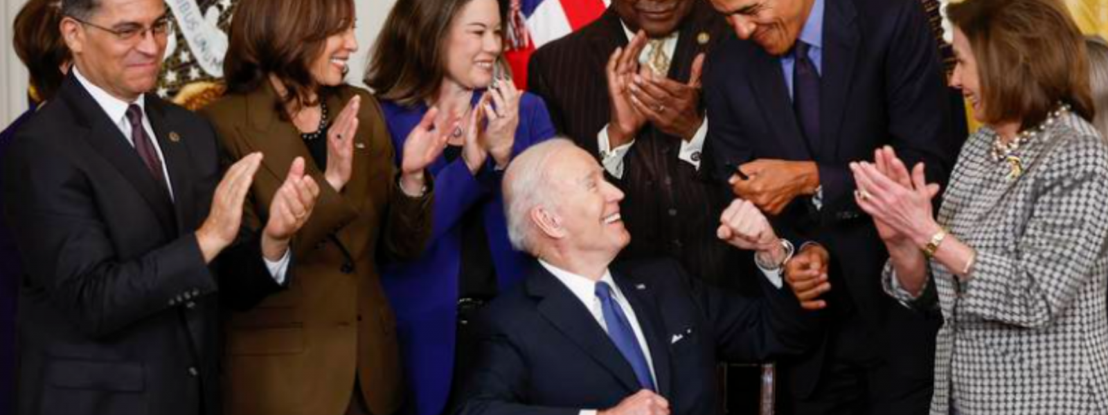 US President Biden seated while shaking President Obama's hand and other national leaders applaud in the background