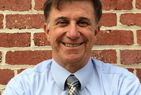 Vincent DeMarco in shirt and tie smiling at the camera in front of a brick wall