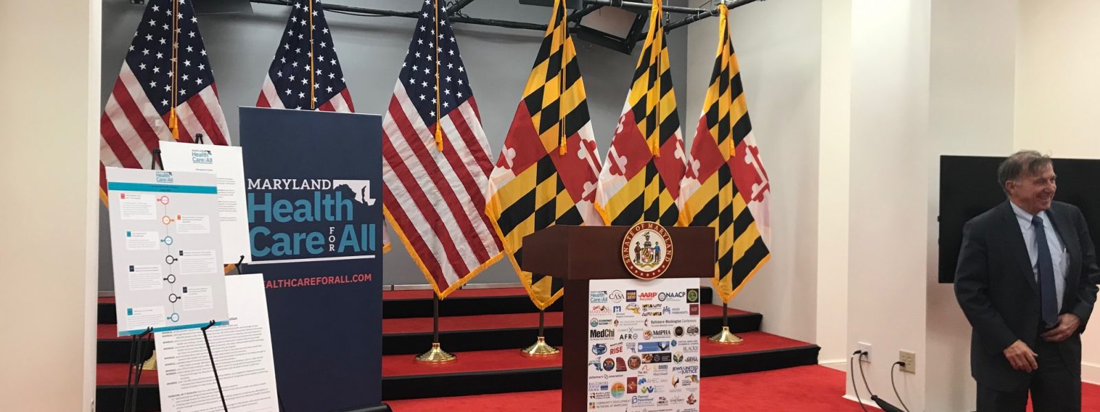 Empty room with Maryland flags, podium, United States flags and posters about the health care agenda